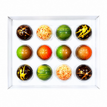 Load image into Gallery viewer, A 12-piece assortment of colorful round chocolates in a clear plastic tray, featuring various patterns of green, orange, yellow, and brown on a white background.