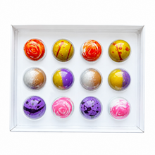 Load image into Gallery viewer, A boxed set of 12 decorative spherical confections or chocolates arranged in a white tray. Each sphere has a different colorful marbled or swirled pattern in red, yellow, purple, pink, brown, and white, photographed on a clean white background.