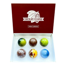 Load image into Gallery viewer, An open red gift box labeled 'Chocolate Escapade' containing six decorative chocolate spheres in assorted colors, photographed on a plain white background.