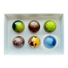 Load image into Gallery viewer, A white rectangular gift box containing six spherical chocolates arranged in two rows of three. The chocolates feature various colorful designs, including green, brown, lime green, yellow with chocolate drizzle, and blue.