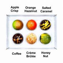 Load image into Gallery viewer, Six gourmet chocolate spheres arranged in a clear square tray on a white background, labeled Apple Crisp, Orange Hazelnut, Salted Caramel, Coffee, Crème Brûlée, and Honey Nut.
