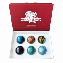 Load image into Gallery viewer, An open red gift box labeled 'Chocolate Escapade' containing six decorative chocolates in assorted blue, brown, black, and yellow patterns, set against a plain white background.
