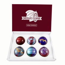 Load image into Gallery viewer, An open white gift box with a dark burgundy lid printed with the brand name 'CHOCOLATE ESCAPADE' and 'Artisan Confections'. Inside are six glossy, spherical decorated chocolates arranged in two rows of three.
